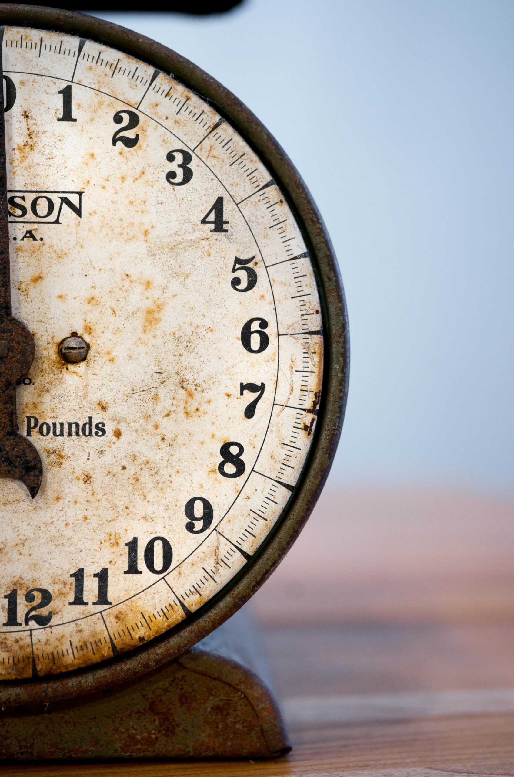 Close-up of a rustic vintage weight scale showing numbers on a weathered dial.